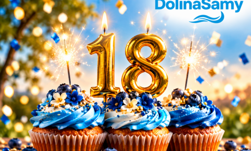 Grafika jubileuszowa z okazji 18-lecia LGD Dolina Samy. Na pierwszym planie znajdują się trzy babeczki ozdobione niebiesko-białym kremem, borówkami i dekoracjami w kolorze niebieskim oraz złotym. Na środkowej babeczce umieszczono duże, złote cyfry „18” ze świeczkami i zimnymi ogniami. W tle widać rozświetlone niebo, zieleń, konfetti oraz efekty świetlne. W prawym górnym rogu znajduje się niebieskie logo „DolinaSamy – Lokalna Grupa Działania” z charakterystycznym symbolem fal.